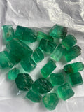 A collection of vivid green Panjshir emeralds of various sizes, displayed on a white background.