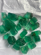 A collection of vivid green Panjshir emeralds of various sizes, displayed on a white background.