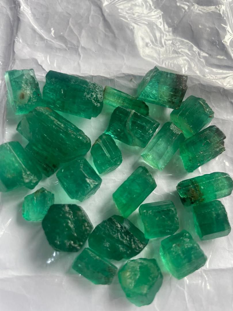 A collection of vivid green Panjshir emeralds of various sizes, displayed on a white background.